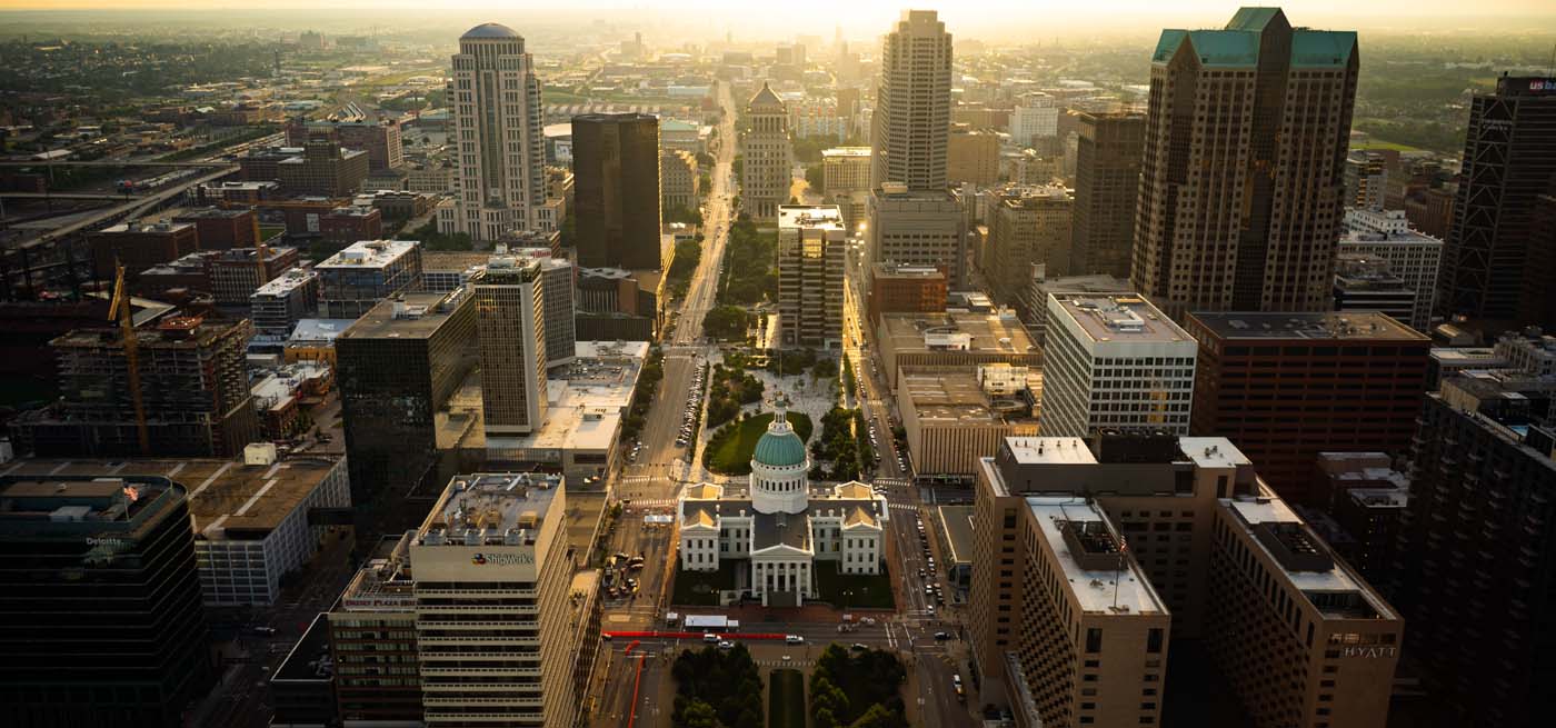 sunset aerial view of downtown saint louis MO commercial real estate buildings with the sun on the horizon in the background and centered on the old courthouse and its blue dome